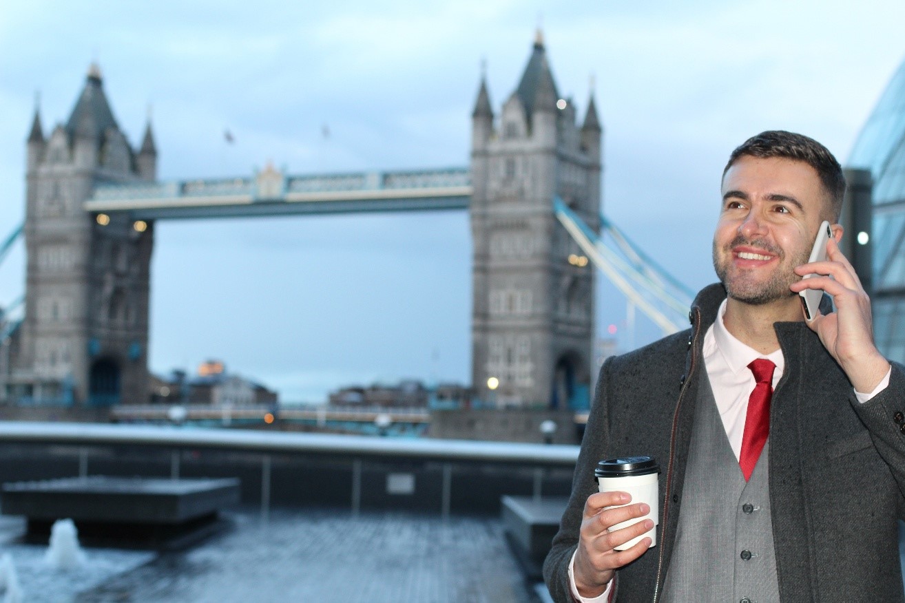 A person in a suit on the phone in front of tower bridge