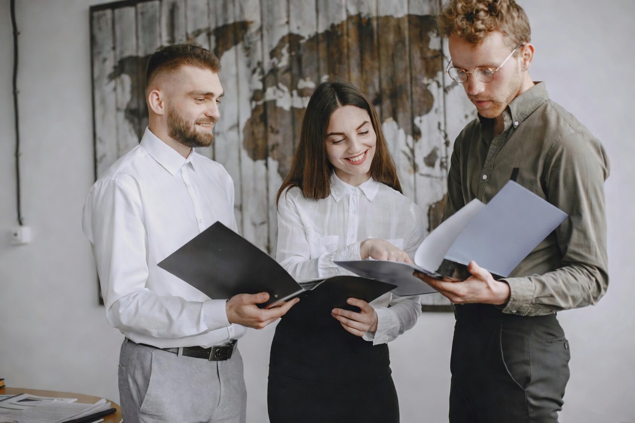 Three people in front of a map looking at some documents